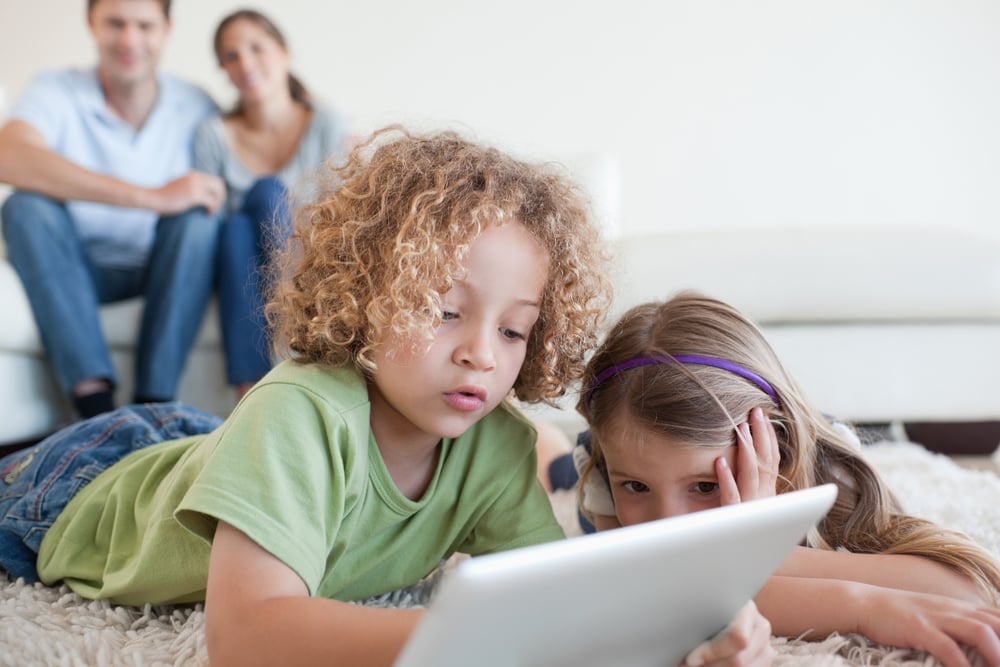 Young children using a tablet computer while their happy parents are watching in their living room